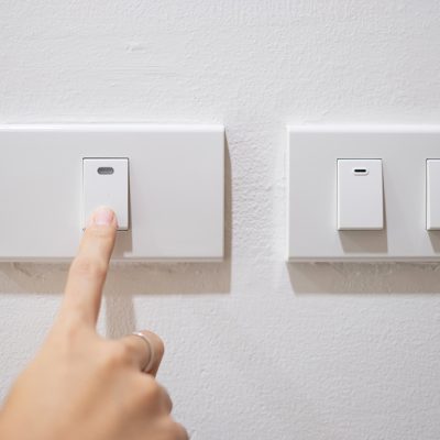 Female finger is turn on or off on light switch on white wall at home. Energy Saving, power, electrical and lifestyle concepts .